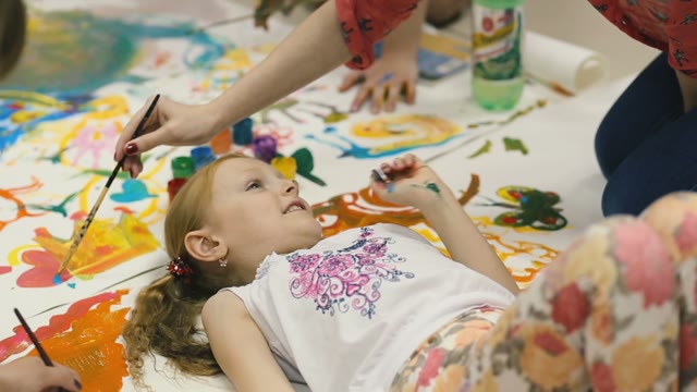 Girl Lying On The Floor Around Her Paint Colors. Put A Blot On His Nose.