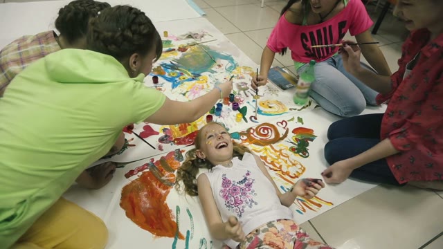 Girl Lying On The Floor And Laughs Around Her Paint Colors.
