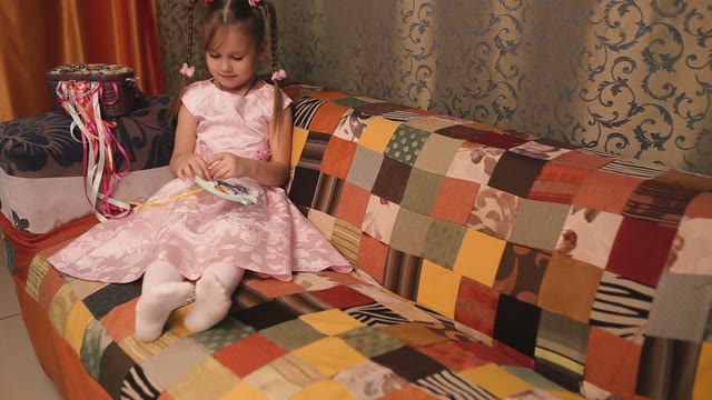 Small Needlewoman In A Pink Dress Sitting On A Sofa And Embroiders.
