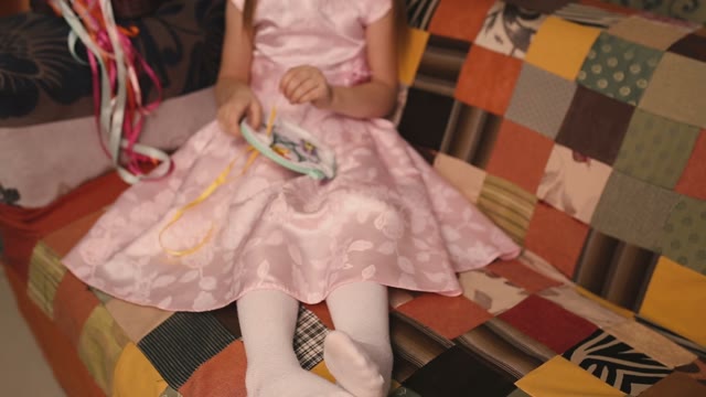 Small Needlewoman In A Pink Dress Sitting On A Sofa And Embroiders.