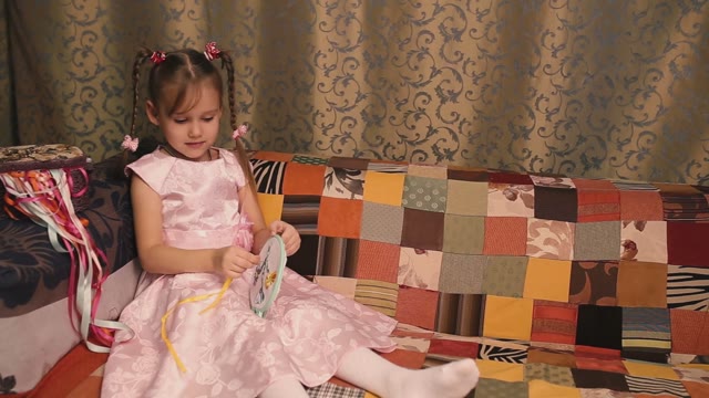 Small Needlewoman In A Pink Dress Sitting On A Sofa And Embroiders.