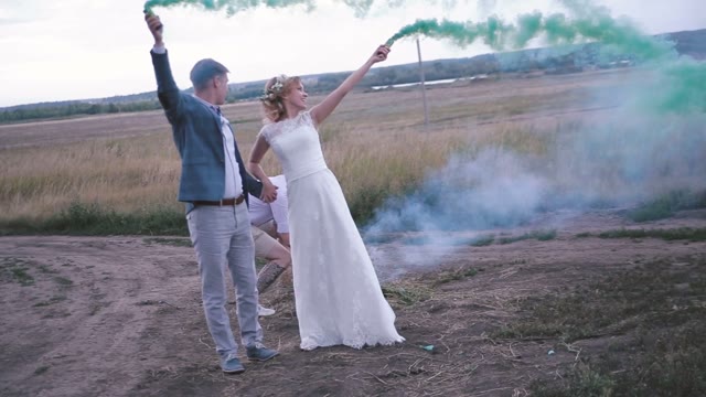 The Bride, The Groom And His Friend Posing In A Field With Smoke Bombs.