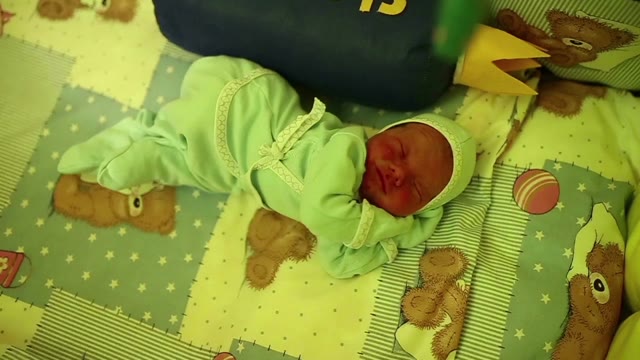 A Newborn Sleeps In A Crib, And Very Cute Stirs In His Sleep.