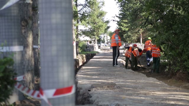 Workers Digging A Trench. Man Rolls Equipment.