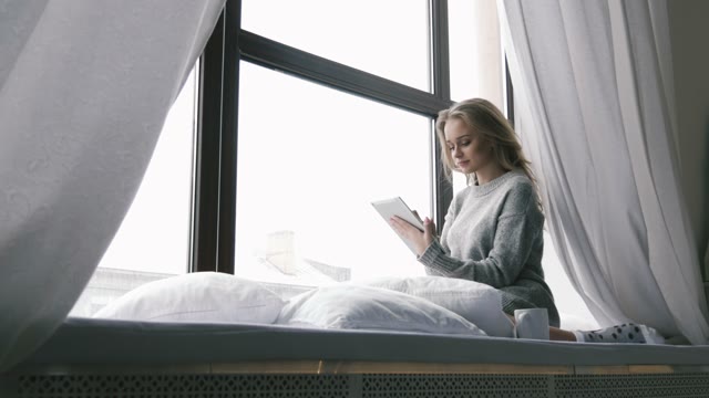 Young Girl Sitting On A Window Sill And Enjoys The Tablet