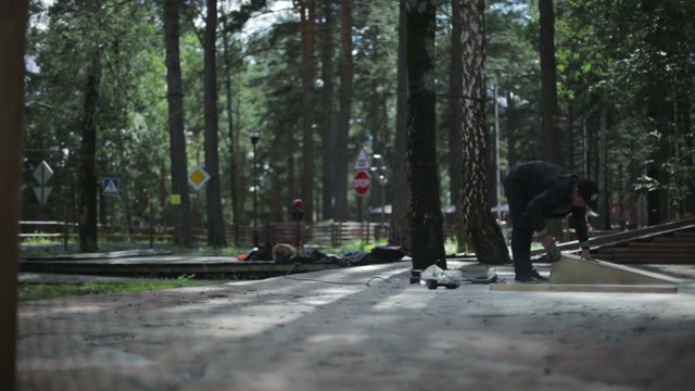 Young Man Polishing A Wooden Springboard. Around The Trees