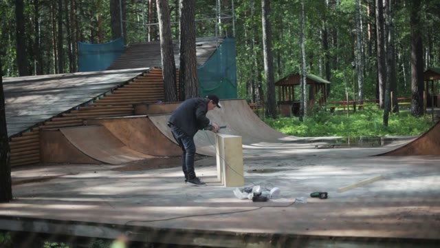 Young Guy Is Building A Springboard Into The Skatepark. Around The Forest