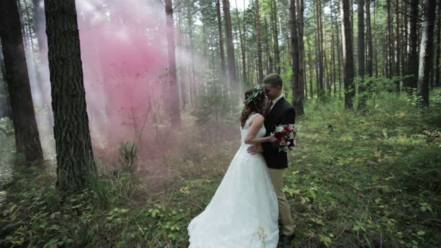 Newlyweds Standing In A Forest In The Midst Of Pink Smoke