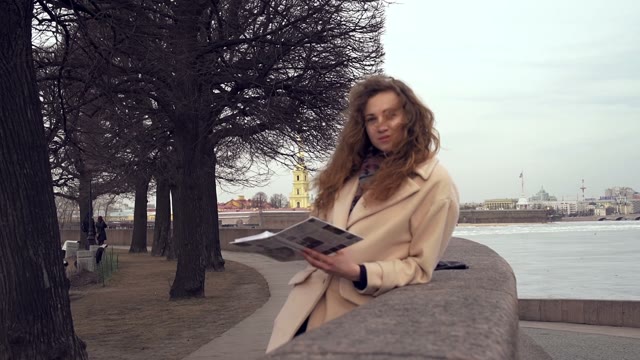 Cute Young Curly Girl Reading A Book On The Embankment Of The River