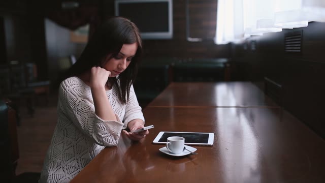 Beautiful Girl With A Phone In Her Hands Sitting In A Coffee Shop