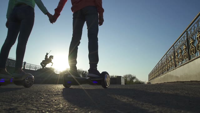 Man And Woman Hold Hands And Ride On Hoverboard