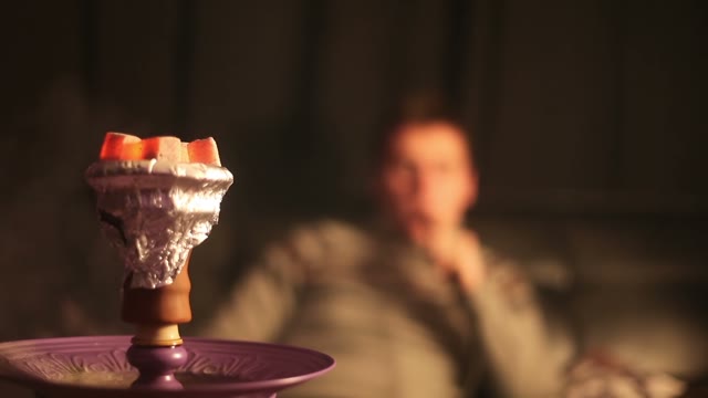 A Man Smokes A Hookah And Exhales. Hookah Charcoal With Which Lights Up In The