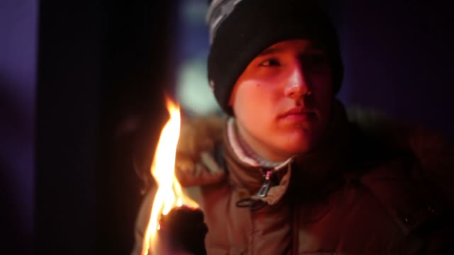 Young Man In Jacket And Hat Holding A Torch Andlooking Somewhere