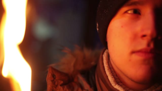 The Young Man In Winter Clothes In The Light Of The Fire Looking At The Camera