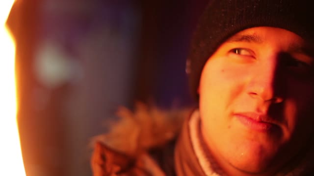 The Young Man In Winter Clothes In The Light Of The Fire Looking At The Camera