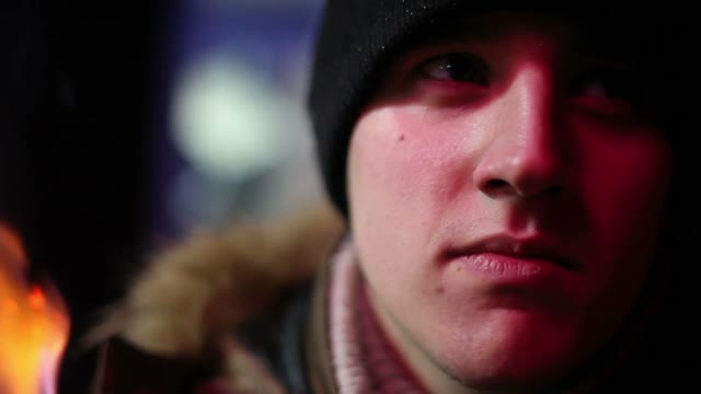 The Young Man In Winter Clothes In The Light Of The Fire Looking At The Camera