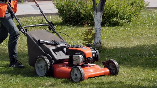 Worker In Uniform Mowing Grass With Lawn Mower