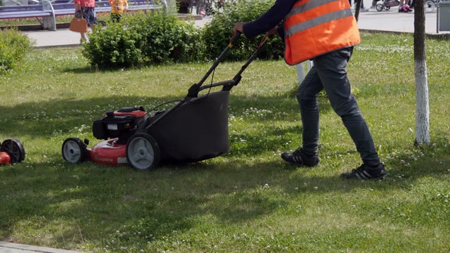 Worker In Uniform Mowing Grass With Lawn Mower