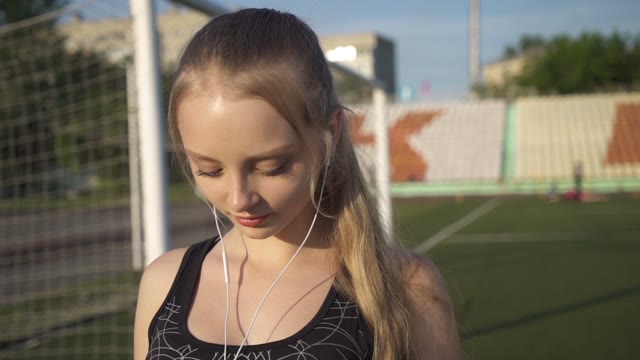 Young Woman Athlete Goes Through The Stadium With Headphones In Their Ears