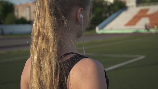Young Woman Athlete Goes Through The Stadium With Headphones In Their Ears