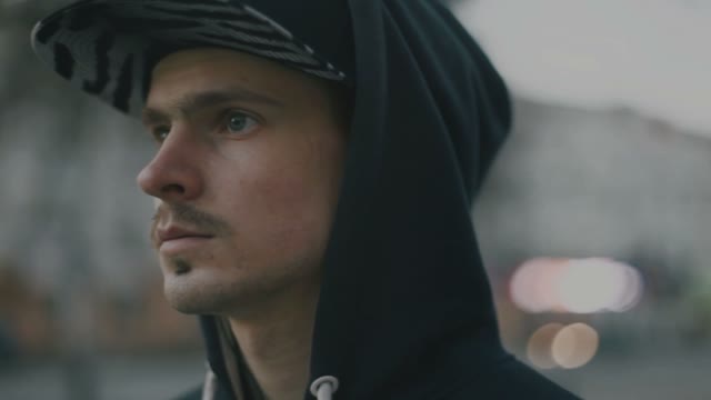 A Young Man In A Cap And Hood Removes The Headphone Out Of The Ear
