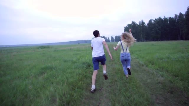 Young Couple Running On The Green Field With A Kite