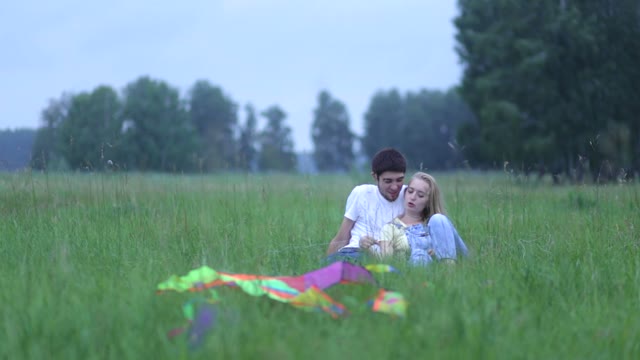 Young Couple In Love Lying On The Grass In The Field, Hugging And Talking.