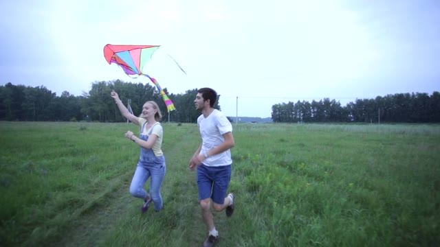 Young Couple Running On The Green Field With A Kite