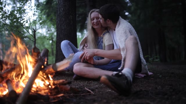 Young Couple Sitting In A Forest Fire. The Guy Kisses The Girl.