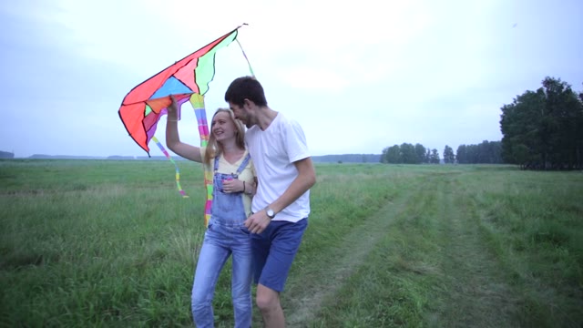 Young Couple In Love Walking On Summer Field And Hugging. The Girl Holding A Kit