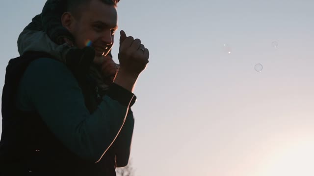 Happy Father With A Child Playing Soap Bubbles At Sunset