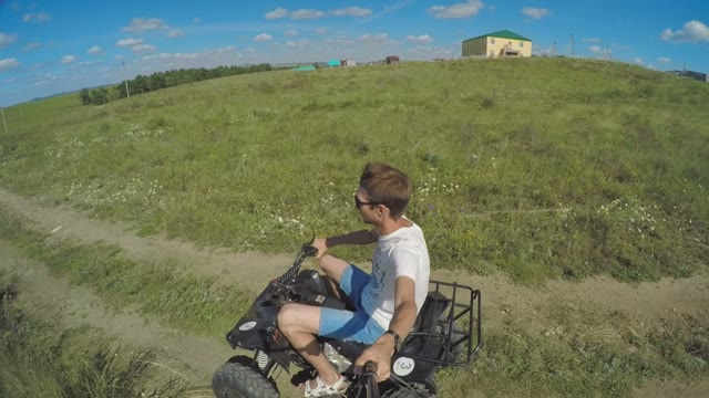 A Young Man Riding A Quad Bike On A Field And Shoots Himself With Selfie Sticks