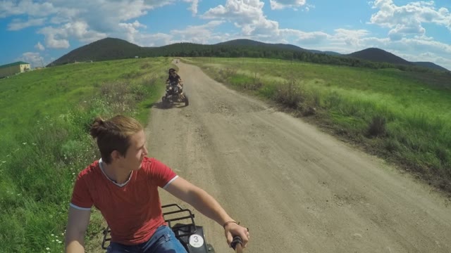 A Young Man Riding A Quad Bike On A Field And Shoots On Selfie Sticks Himself