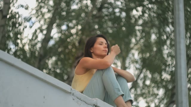 A Girl Sits On A Ledge On A Background Of Trees