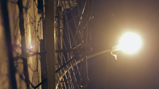 Large Fence With Barbed Wire At Night Lit By A Lantern