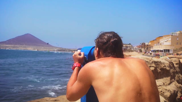 Man Looking Through Binoculars On The Coast Of The Blue Sea