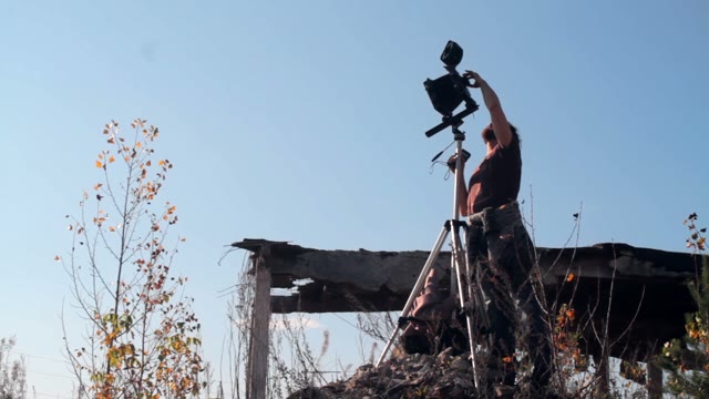 Man Adjusts The Retro Camera Among The Ruins