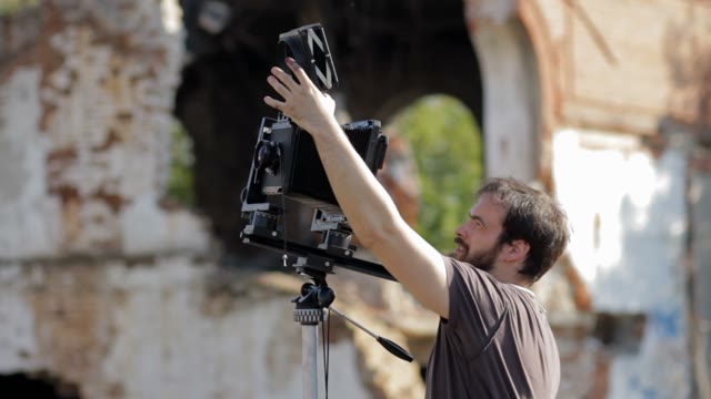 Man Adjusts The Retro Camera Among The Ruins