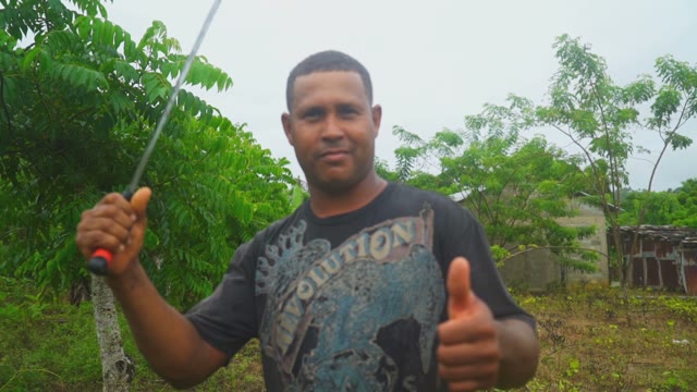 The Farmer With A Machete Shows Thumb In A Large Green Forest