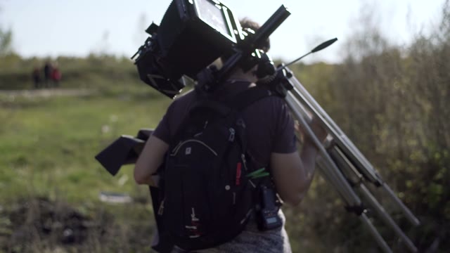 Man Walks With A Retro Camera Among Green Bushes