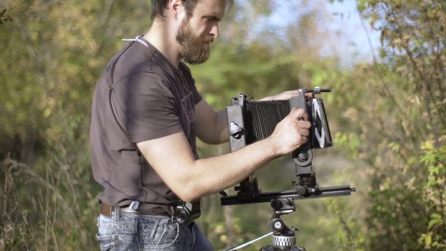 Man Puts A Retro Camera Among Green Trees