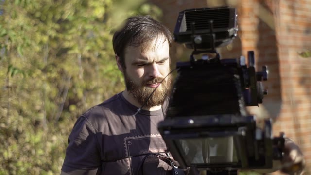 Man Puts A Retro Camera Among Green Trees Close-up