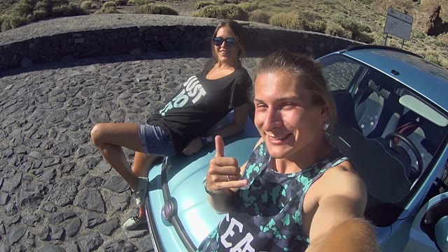Young Couple Filming Themselves Outdoors Sitting On Car