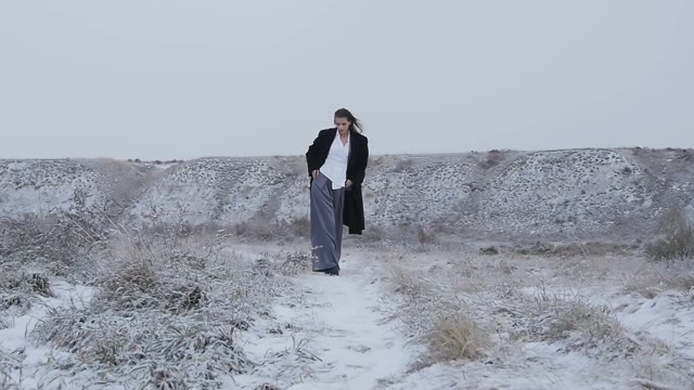 The Girl In A Strict Suit And A Black Coat Walking On Snow-covered Mountains