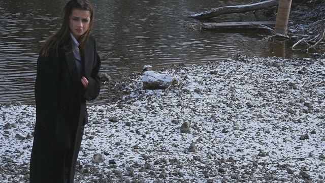 Woman In A Long Black Coat In The Snow Near The River