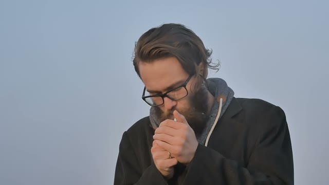 Tall Guy Lights A Cigarette And Smokes On A Background Of Blue Sky