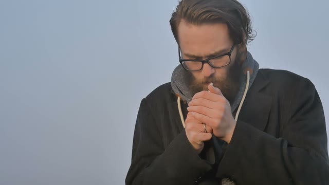 Man Lights A Cigarette And Smokes On A Background Of Blue Sky