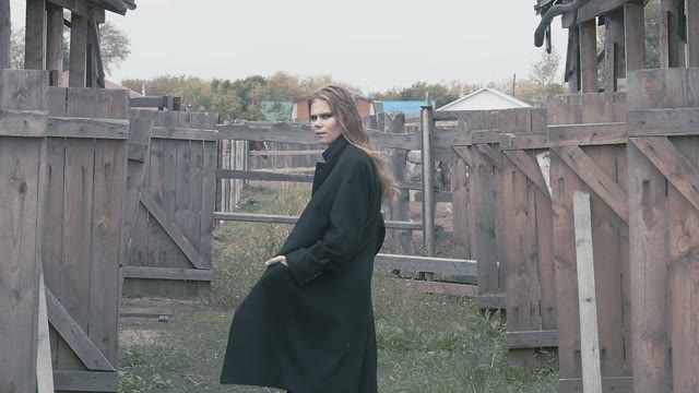 Beautiful Girl In A Black Coat Against The Background Of The Village Fence