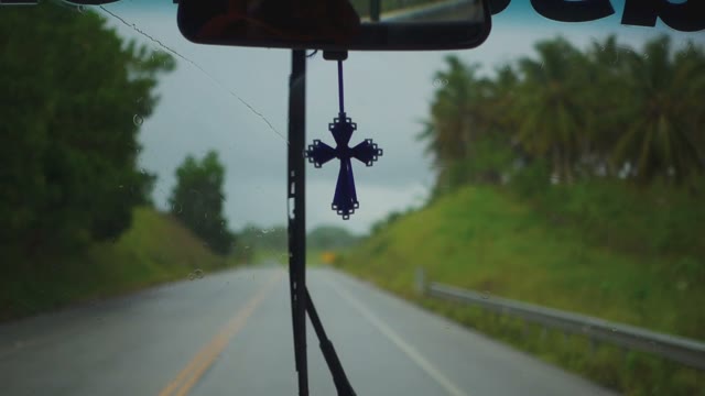 Windshield Wipers And A Cross On The Mirror Inside The Car Rides On A Wet Road