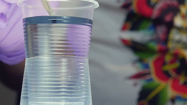 Man Pouring Black Paint In A Plastic Cup With Water Close-up